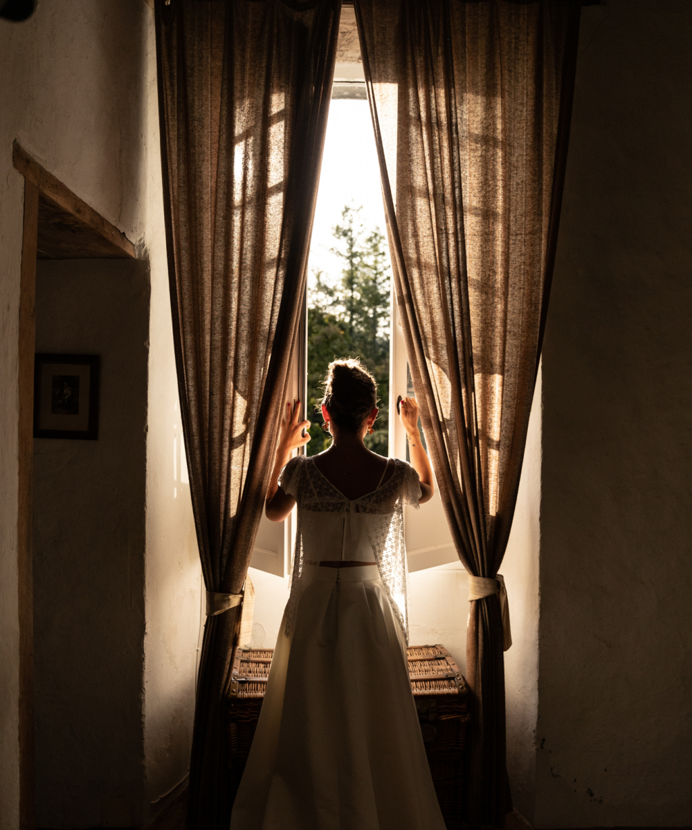 La lumière qui passe au travers de cette fenêtre en fin de journée viens joliment détourer la belle mariée et sa belle robe de mariée bohème